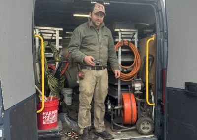 Plumber standing in the open rear of a service van with drain equipment