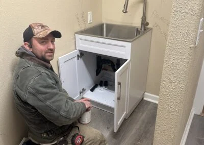 Plumber kneeling beside an open white vanity sink during installation
